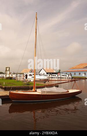 Un petit voilier amarré à la marina de Potter Heigham, Norfolk Broads, Angleterre Royaume-Uni avec ses voiles vers le bas Banque D'Images