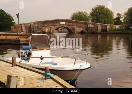 Une vue sur le pont Potter Heigham et la marina sur la rivière Thurne, avec un petit bateau de croisière le long du poste d'amarrage. Norfolk Broads, Angleterre, Royaume-Uni Banque D'Images