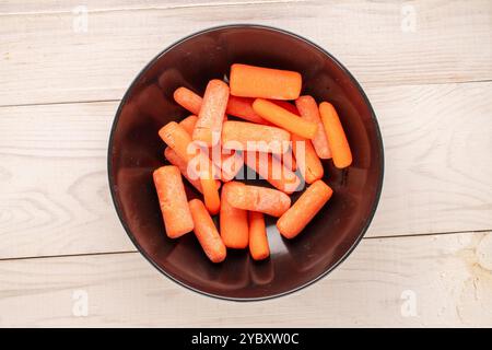 Petite carotte pelée avec plat en céramique et couteau sur table en bois, macro, vue de dessus. Banque D'Images