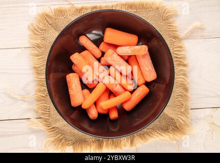 Petite carotte pelée avec plat en céramique et couteau sur table en bois, macro, vue de dessus. Banque D'Images