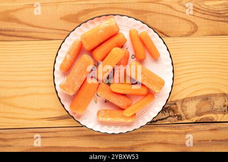 Petite carotte pelée avec plat en céramique et couteau sur table en bois, macro, vue de dessus. Banque D'Images