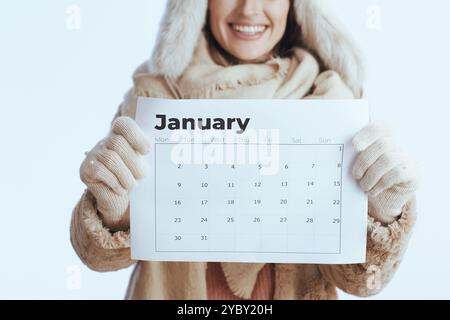 heureuse femme moderne de 40 ans en manteau d'hiver et chapeau de fourrure isolé sur blanc dans des gants blancs avec calendrier de janvier. Banque D'Images