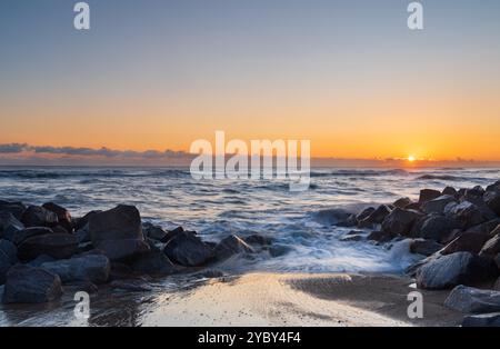 Sea Defence roches sur la plage alors que le soleil se levait à Mundesley, Norfolk, Royaume-Uni avec une longue exposition pour lisser l'eau Banque D'Images