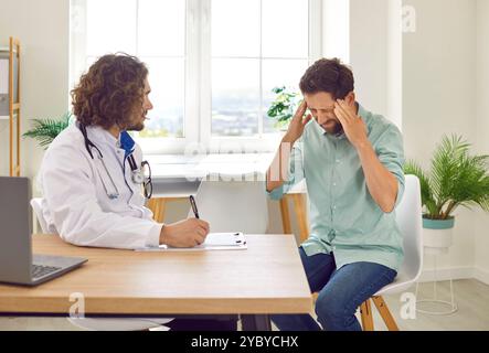 Patient stressé masculin assis dans le cabinet du médecin en clinique médicale souffrant de céphalées. Banque D'Images