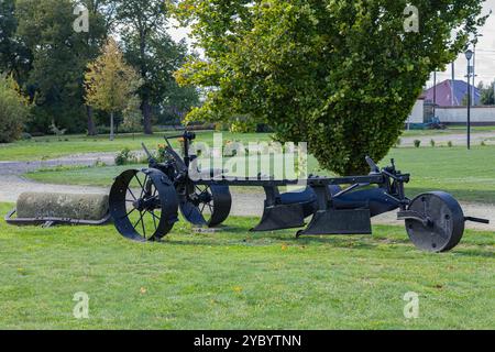 Charrue agricole vintage avec de grandes roues affichées sur un champ herbeux dans un parc entouré d'arbres par une journée ensoleillée Banque D'Images