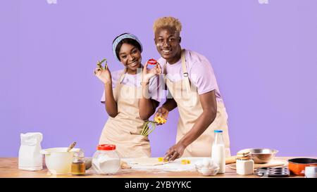Jolie petite amie africaine américaine et petit ami faisant des biscuits sur fond lilas Banque D'Images