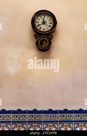 horloge vintage avec des chiffres romains accrochés sur un mur jaune décoré de carreaux bleus Banque D'Images