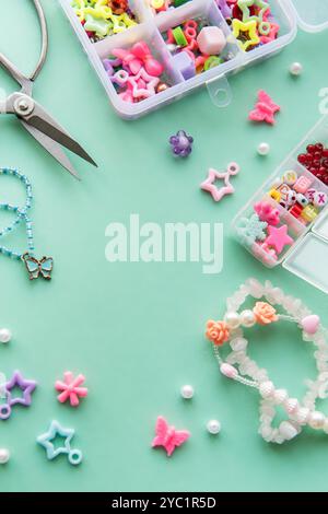 Des matériaux d'artisanat, y compris des perles colorées et des breloques, sont organisés dans des conteneurs sur une surface vert menthe, avec des ciseaux prêts à faire des jewe uniques Banque D'Images