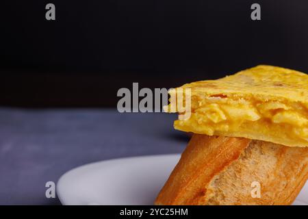 Brochette d'omelette espagnole partiellement visible sur une table en béton bleuâtre. Capturé d'en haut, mettant en valeur la texture de la tortilla traditionnelle de p Banque D'Images