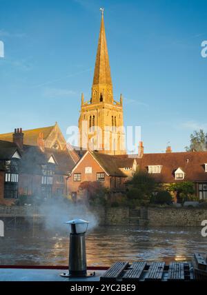 Péniche amarrée au bord de la Tamise à Abingdon. Une belle vue sur la Tamise à Abingdon, tôt un matin d'automne brumeux. Nous sommes sur la rive sud de la rivière, regardant en face de la belle église anglo-saxonne de St Helens, il fait froid le matin, donc la péniche au premier plan a allumé son feu pour un peu de chaleur... Banque D'Images