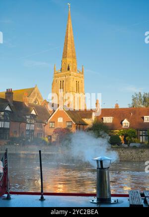 Péniche amarrée au bord de la Tamise à Abingdon. Une belle vue sur la Tamise à Abingdon, tôt un matin d'automne brumeux. Nous sommes sur la rive sud de la rivière, regardant en face de la belle église anglo-saxonne de St Helens, il fait froid le matin, donc la péniche au premier plan a allumé son feu pour un peu de chaleur... Banque D'Images