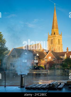 Péniche amarrée au bord de la Tamise à Abingdon. Une belle vue sur la Tamise à Abingdon, tôt un matin d'automne brumeux. Nous sommes sur la rive sud de la rivière, regardant en face de la belle église anglo-saxonne de St Helens, il fait froid le matin, donc la péniche au premier plan a allumé son feu pour un peu de chaleur... Banque D'Images