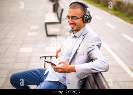 Portrait d'homme d'affaires heureux qui est la messagerie sur smartphone. Homme assis sur un banc dans la ville et utilisant un smartphone. Banque D'Images