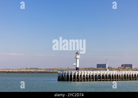 Un phare pittoresque se dresse fièrement sur une jetée en bois, surplombant les eaux sereines et calmes par une journée ensoleillée Banque D'Images
