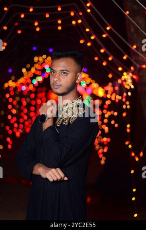 Un enfant du village bangladais portant du punjabi rouge est photographié au milieu des lumières de la nuit. Banque D'Images