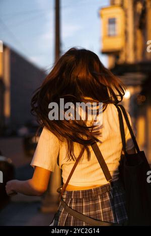 Une jeune femme marche à travers la ville dans la lumière dorée du coucher du soleil. Banque D'Images