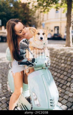 Femme joue avec son chien Corgi sur un cyclomoteur Vespa un jour ensoleillé Banque D'Images