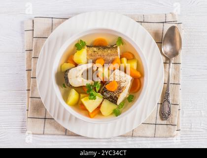 Soupe claire de brochet avec légumes, persil et épices dans un bol blanc sur une table en bois blanc avec cuillère, vue horizontale d'en haut, gros plan, plat Banque D'Images