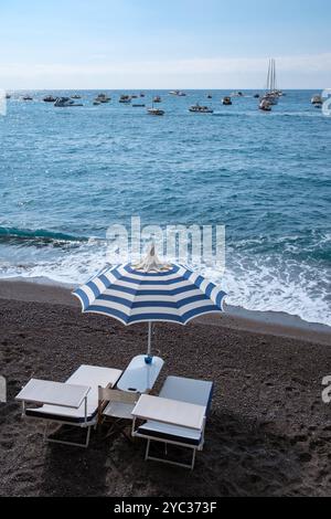 Les visiteurs profitent d'une journée sereine à la plage sous des parasols rayés, en savourant les vagues douces et les superbes vues côtières. Les voiliers parsèment l'étincelle Banque D'Images