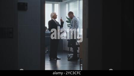 Dans le bureau moderne de la banque ou de la société financière : patron en colère crie à l'employé de la société sur l'affaire infructueuse, jette des papiers et laisse. L'homme stressé s'assoit sur le lieu de travail. Ralenti. Banque D'Images