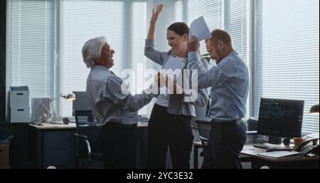 Dans la salle de bureau moderne de l'entreprise : équipe heureuse et excitée d'employés ou de commerçants divers de l'entreprise se réjouissant, applaudissant et célébrant un accord commercial ou une stratégie d'investissement réussie. Ralenti. Banque D'Images
