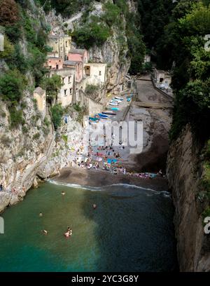 Prélasser dans la chaleur du soleil italien, les visiteurs se détendent sur la plage de galets d'une crique cachée le long de la côte amalfitaine. Des bateaux colorés reposent sur le rivage Banque D'Images