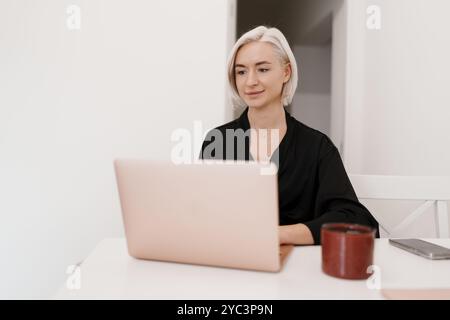 Femme concentrée travaillant sur ordinateur portable à la maison dans la cuisine Banque D'Images