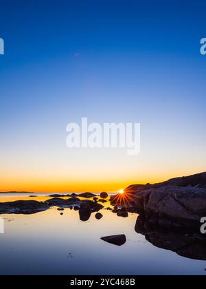 Un coucher de soleil à couper le souffle jette une lueur chaude sur la côte suédoise, illuminant les eaux calmes. Les roches silhouettées créent une atmosphère sereine comme Day tran Banque D'Images