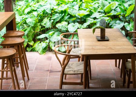 Une salle à manger extérieure confortable avec une table en bois et des chaises entourées d'un feuillage vert luxuriant. Le cadre est serein et accueillant, parfait pour en profiter Banque D'Images