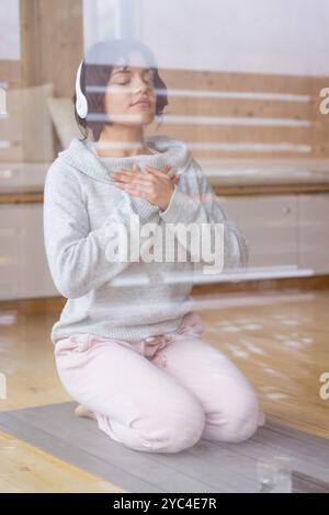 Méditer à la maison, femme portant des écouteurs, trouver la paix dans un moment calme Banque D'Images