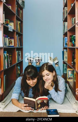 Romny, Ukraine, le 29 septembre 2019 : de jeunes femmes attirantes sont allongées sur le sol entre les étagères d'une ancienne bibliothèque atmosphérique et lisent un livre Banque D'Images