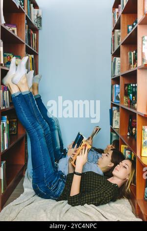 Romny, Ukraine, le 29 septembre 2019 : de jeunes femmes attirantes sont allongées sur le sol entre les étagères d'une ancienne bibliothèque atmosphérique et lisent un livre Banque D'Images