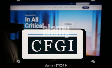 Personne tenant le téléphone portable avec le logo de la société de conseil américaine CFGI sur l'écran en face de la page Web de l'entreprise. Concentrez-vous sur l'affichage du téléphone. Banque D'Images