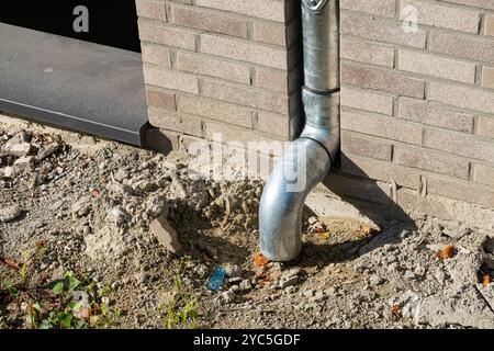 Un tuyau de descente métallique se connecte au sol, canalisant l’eau de pluie loin des fondations d’un bâtiment, assurant un drainage adéquat et empêchant les dommages causés par l’eau Banque D'Images