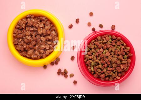 Nourriture humide et sèche pour animaux de compagnie dans des bols d'alimentation sur fond rose. Vue de dessus Banque D'Images