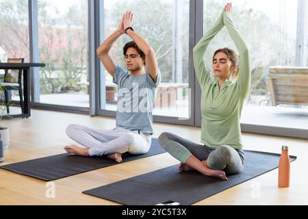 Couple pratiquant le yoga à la maison, méditant sur des tapis avec des expressions pacifiques Banque D'Images