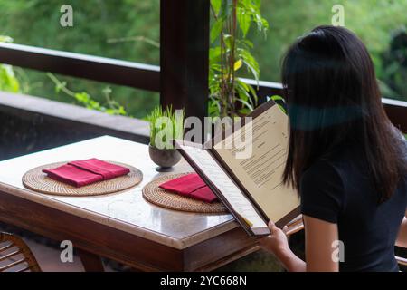 Une table de salle à manger magnifiquement sertie avec deux sets de table ronds tissés, chacun avec une serviette rouge soigneusement pliée. Un petit pot d'herbe verte ajoute une touche de Banque D'Images