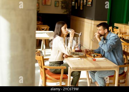 Deux personnes savourent leurs boissons à une table en bois, immergées dans une ambiance de restaurant détendue, tout en étant profondément dans la conversation et les rires. Banque D'Images