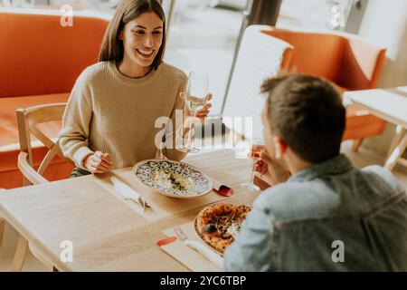 Deux personnes savourent leurs boissons à une table en bois, immergées dans une ambiance de restaurant détendue, tout en étant profondément dans la conversation et les rires. Banque D'Images