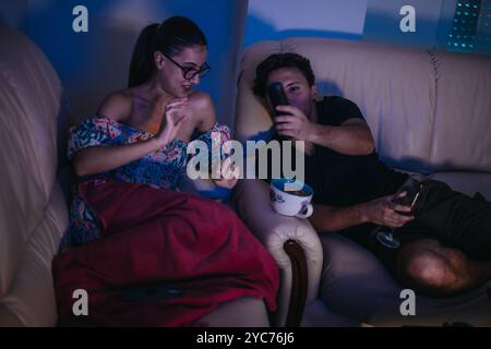 Jeune couple se relaxant avec des collations tout en regardant la télévision ensemble Banque D'Images