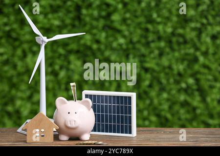 Modèle d'éolienne avec tirelire, figurine de maison et panneau solaire portable sur table à l'extérieur. Concept d'énergie verte Banque D'Images