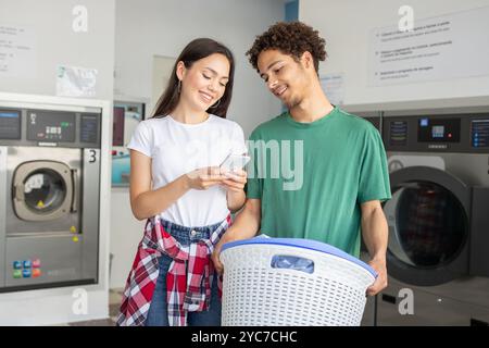 Jeune couple partage un moment dans une laverie automatique tout en faisant la lessive ensemble Banque D'Images