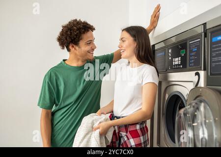 Jeune couple partageant un moment joyeux tout en faisant la lessive dans une laverie moderne Banque D'Images