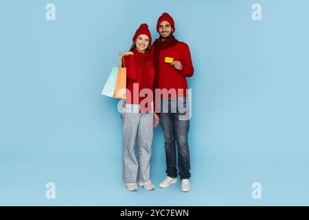 Un couple heureux pose ensemble, présentant des sacs à provisions colorés et une carte-cadeau Banque D'Images