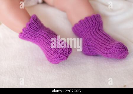 Une paire de minuscules pieds de bébé est vue dans des chaussettes violettes tricotées à la main confortables, reposant confortablement sur un tissu crème doux, évoquant la chaleur et l'innocence pendant un calme Banque D'Images