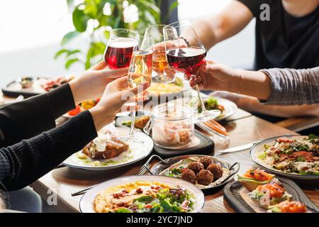 Amis se réunissant à une terrasse de café dans la soirée. Divers jeunes élevant, grillant et fixant des verres avec du vin et du champagne, Cele Banque D'Images