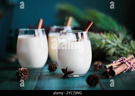 Trois verres de lait de poule crémeux avec des bâtonnets de cannelle et étoile d'anis. Mise au point sélective avec arrière-plan festif flou. Banque D'Images