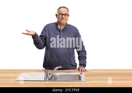 Homme mature confus derrière un évier de cuisine isolé sur fond blanc Banque D'Images