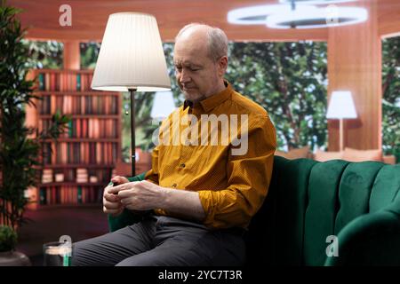 Homme âgé appliquant du sérum et de la crème hydratante sur ses joues, dorlotant la routine quotidienne de soins de la peau pour préserver la peau vieillissante. Personne utilisant la lotion rajeunissante pour le toilettage, soins personnels. Banque D'Images