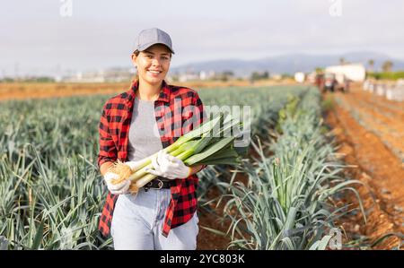 Jeune horticultrice femelle réussie tenant des poireaux récoltés dans le champ Banque D'Images